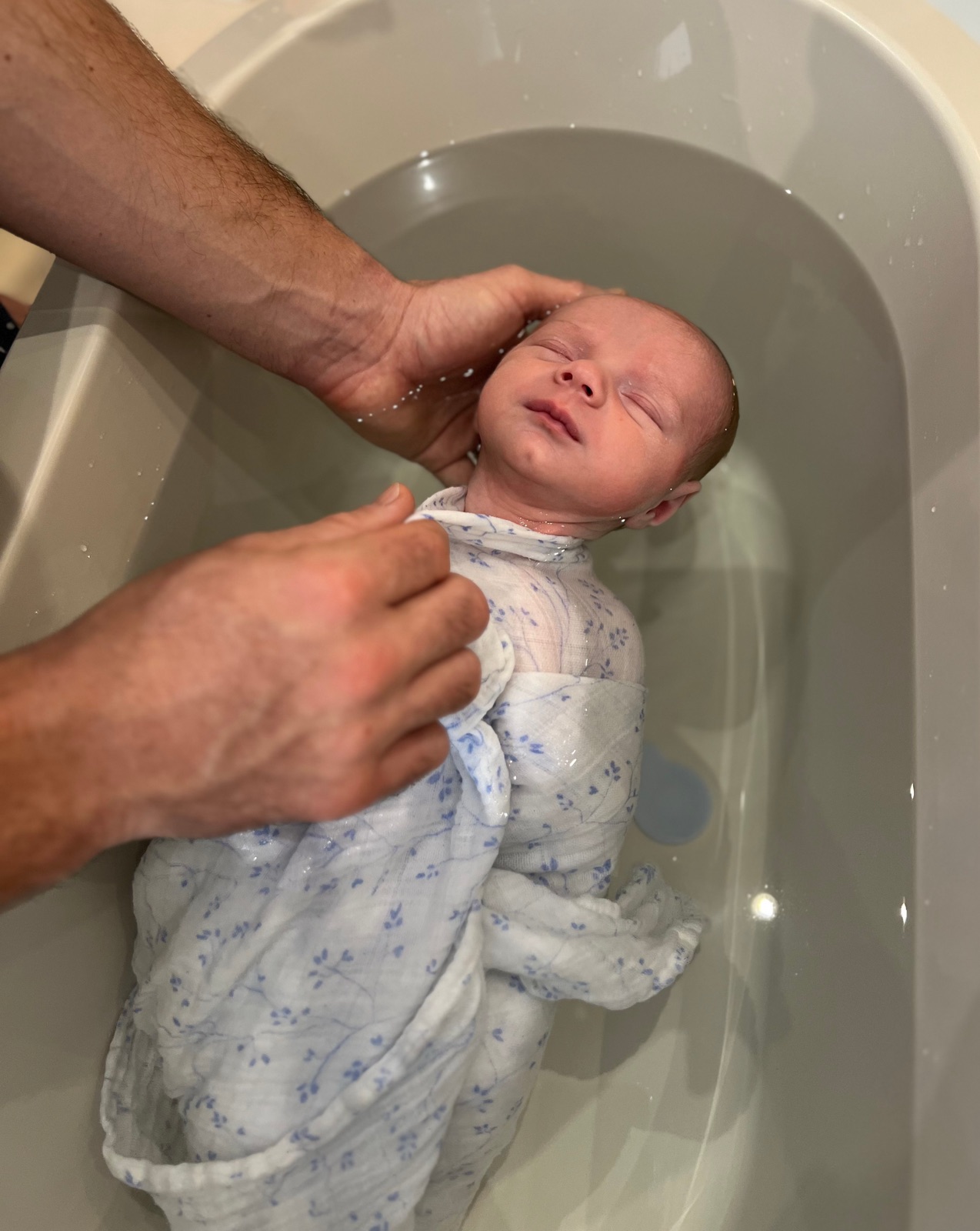 Bébé endormi dans son lange fleuri pendant le bain